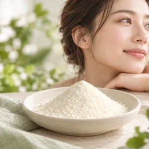 Fine pale powder in a ceramic dish beside pale tubular tissue and a woman’s profile against a muted sage background.